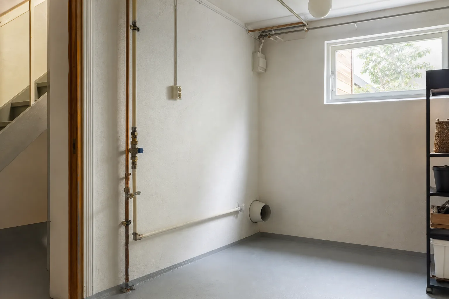 Tomt hörn i ett svenskt villapannrum med inkommande vattenrör, eluttag och ett ventilationsrör mot ytterväggen